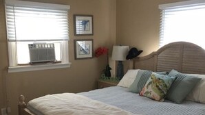 Una camera da letto con un letto in legno, due comodini, un tavolino e una finestra con persiane, oltre a un condizionatore d'aria a parete.