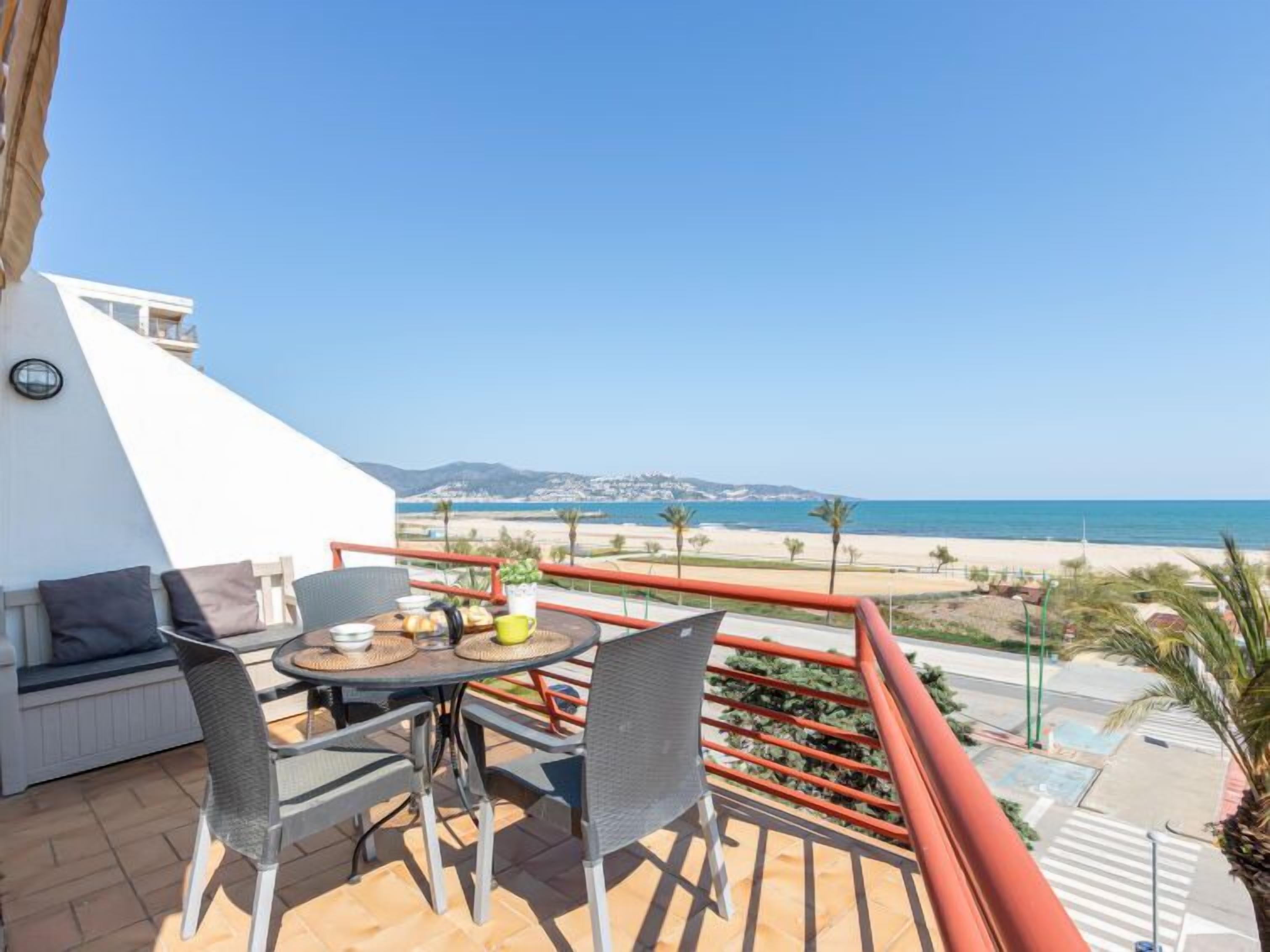 Un balcon avec une table et des chaises, donnant sur une plage et l’océan.