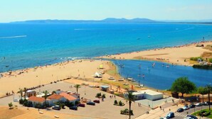 Una zona costera con playa, un puerto deportivo y algunos edificios.