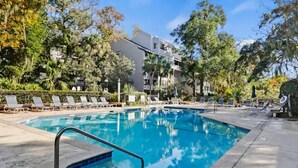 A rectangular swimming pool with a metal ladder, surrounded by lounge chairs and palm trees.