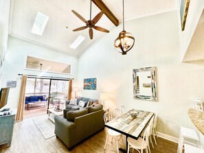 A spacious living area with a ceiling fan, a dining table with chairs, a sofa, and a view of the outside balcony.