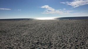 A wide sandy beach with a clear sky and the sun shining.
