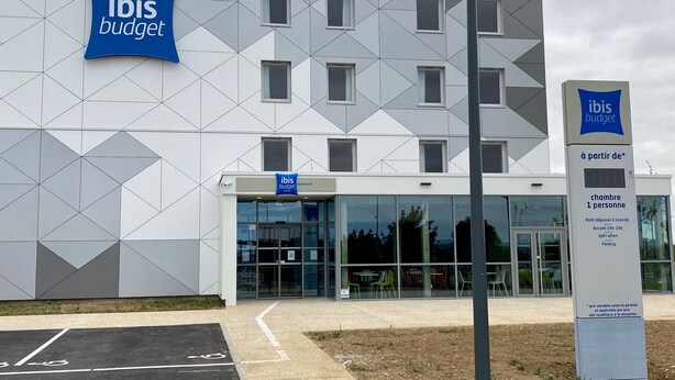 Een modern gebouw met een geometrisch gevelontwerp en een bordje waarop staat dat het een ibis budget hotel is.