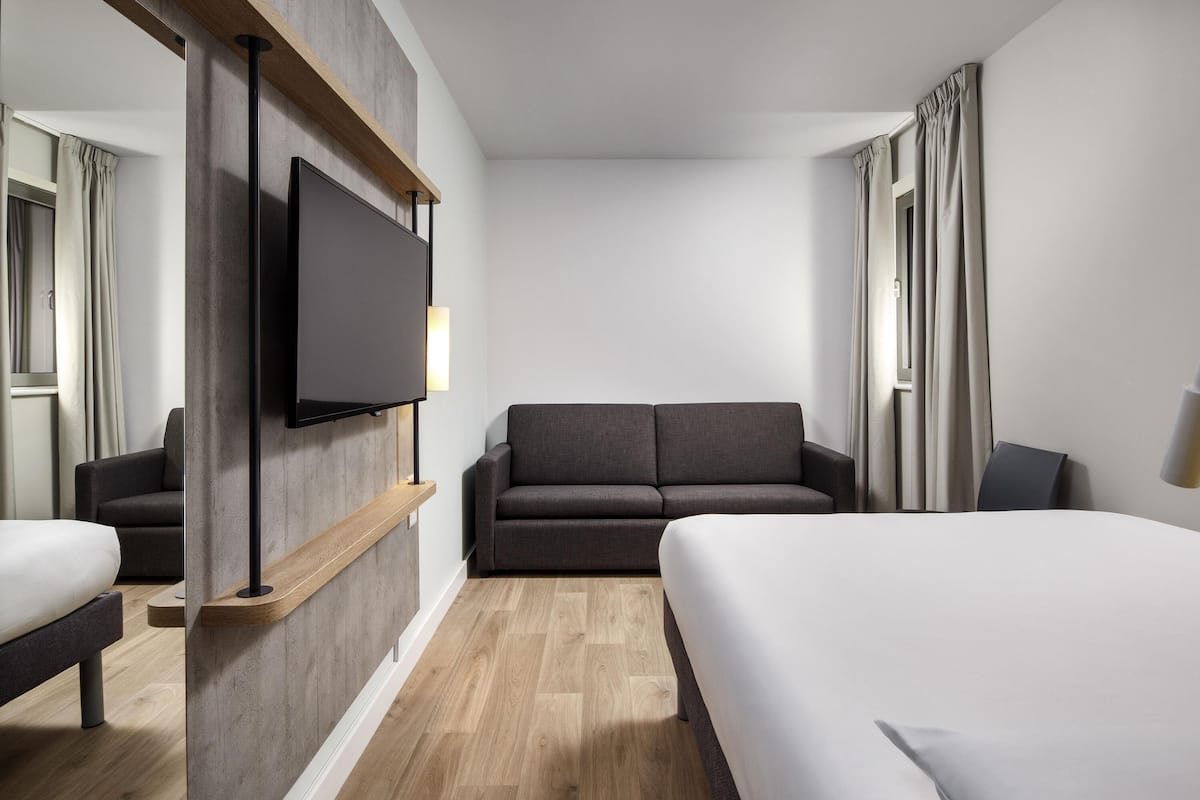 Ein Hotelzimmer mit einem Bett, einer Couch, einem Fernseher und Holzboden.