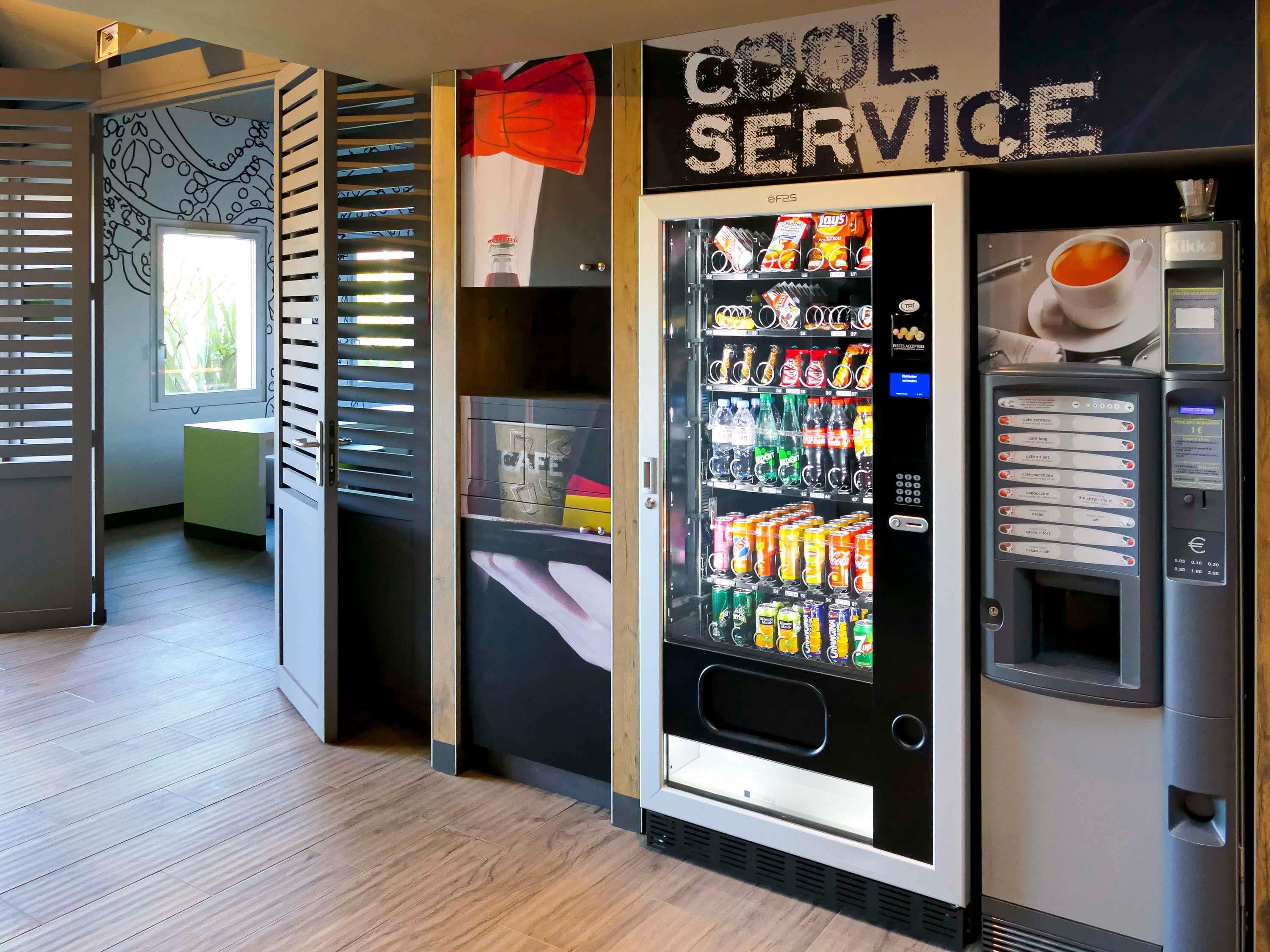 Zona con máquinas expendedoras que incluye un dispensador de bebidas y una máquina de aperitivos, con un rótulo que dice 'COOL SERVICE'.