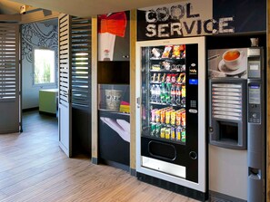 Ein Automatenbereich mit einem Schild, das 'COOL SERVICE' anzeigt, einem Getränkeautomaten und einem Snackautomaten.