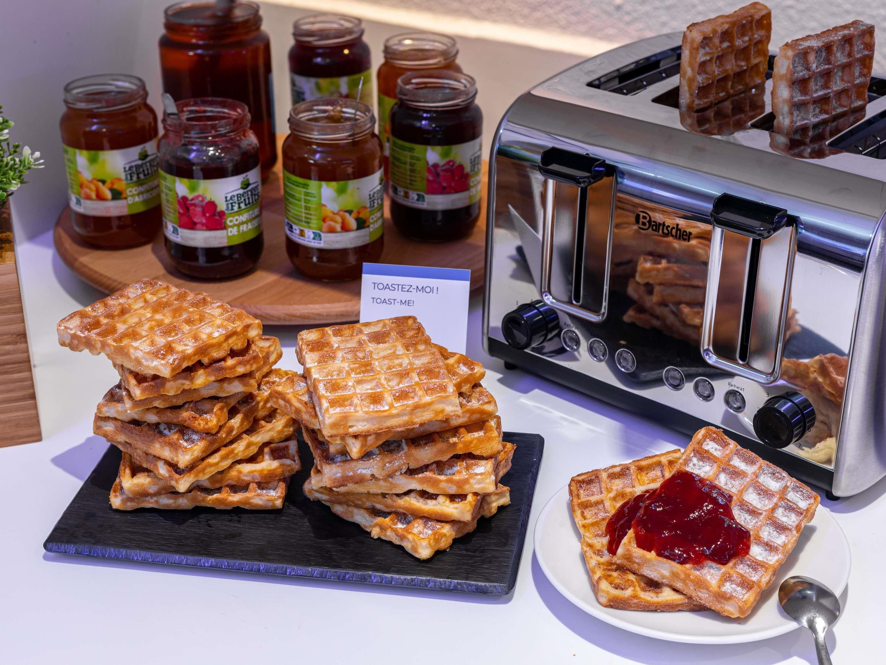 A toaster, waffle stacks, and jam jars on a table.
