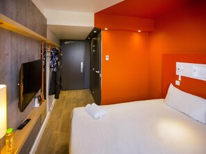 Een hotelkamer met een bed, een televisie, een kapstok en een deur naar een andere kamer.