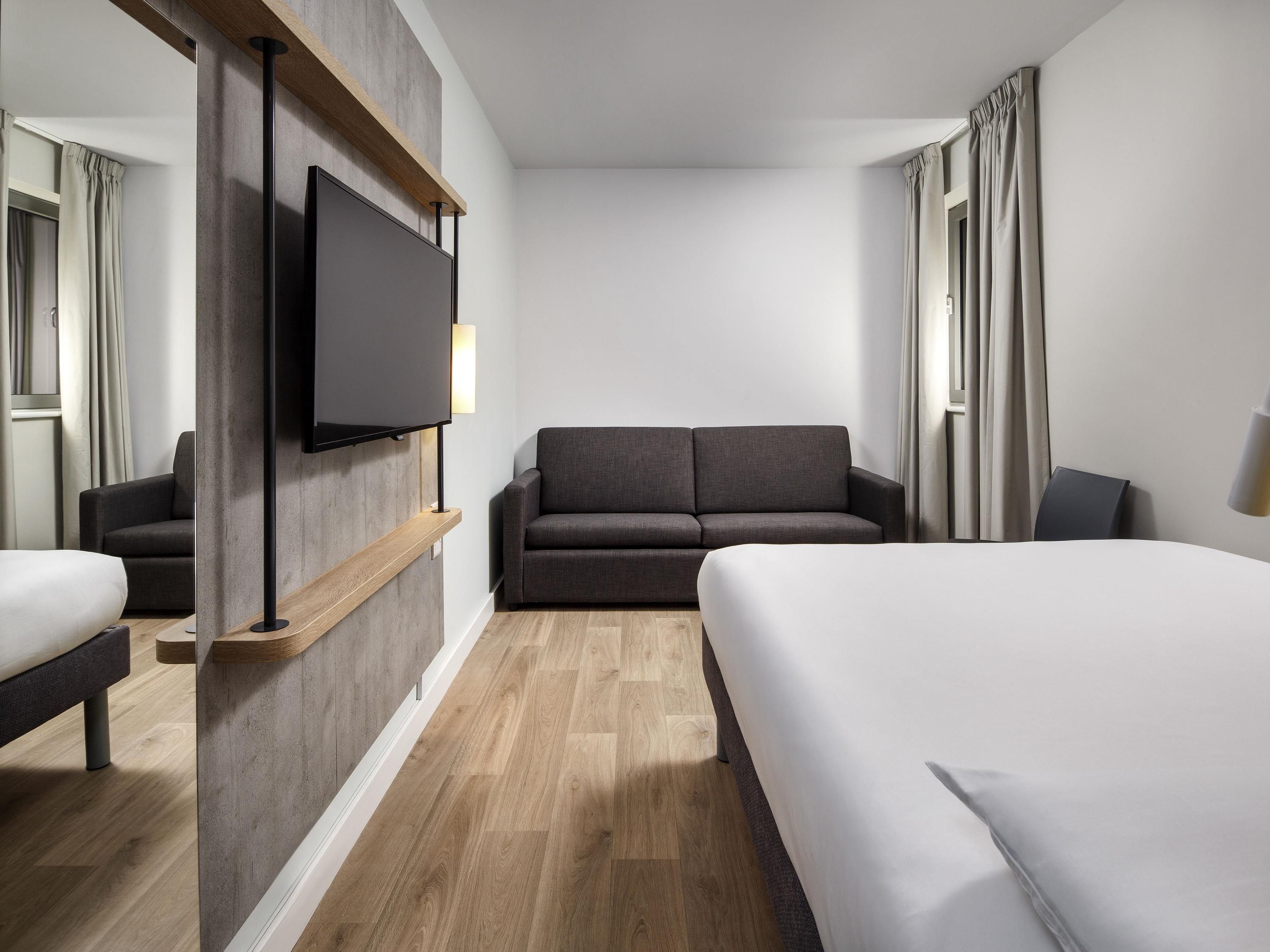 Habitación de hotel con cama, sofá, televisión y suelo de madera.