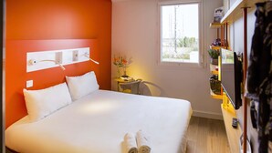 Une chambre d’hôtel avec un grand lit, une petite table avec une chaise, une télévision et une fenêtre donnant sur un immeuble.