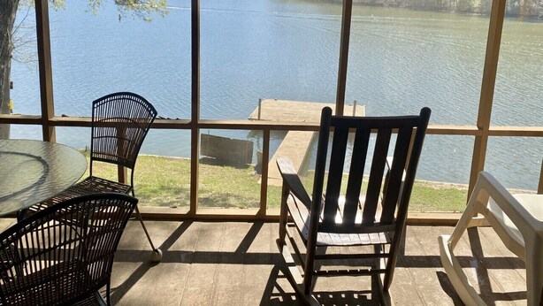 Vista desde una habitación con ventanas amplias que dan a un lago, con una mesa y sillas.