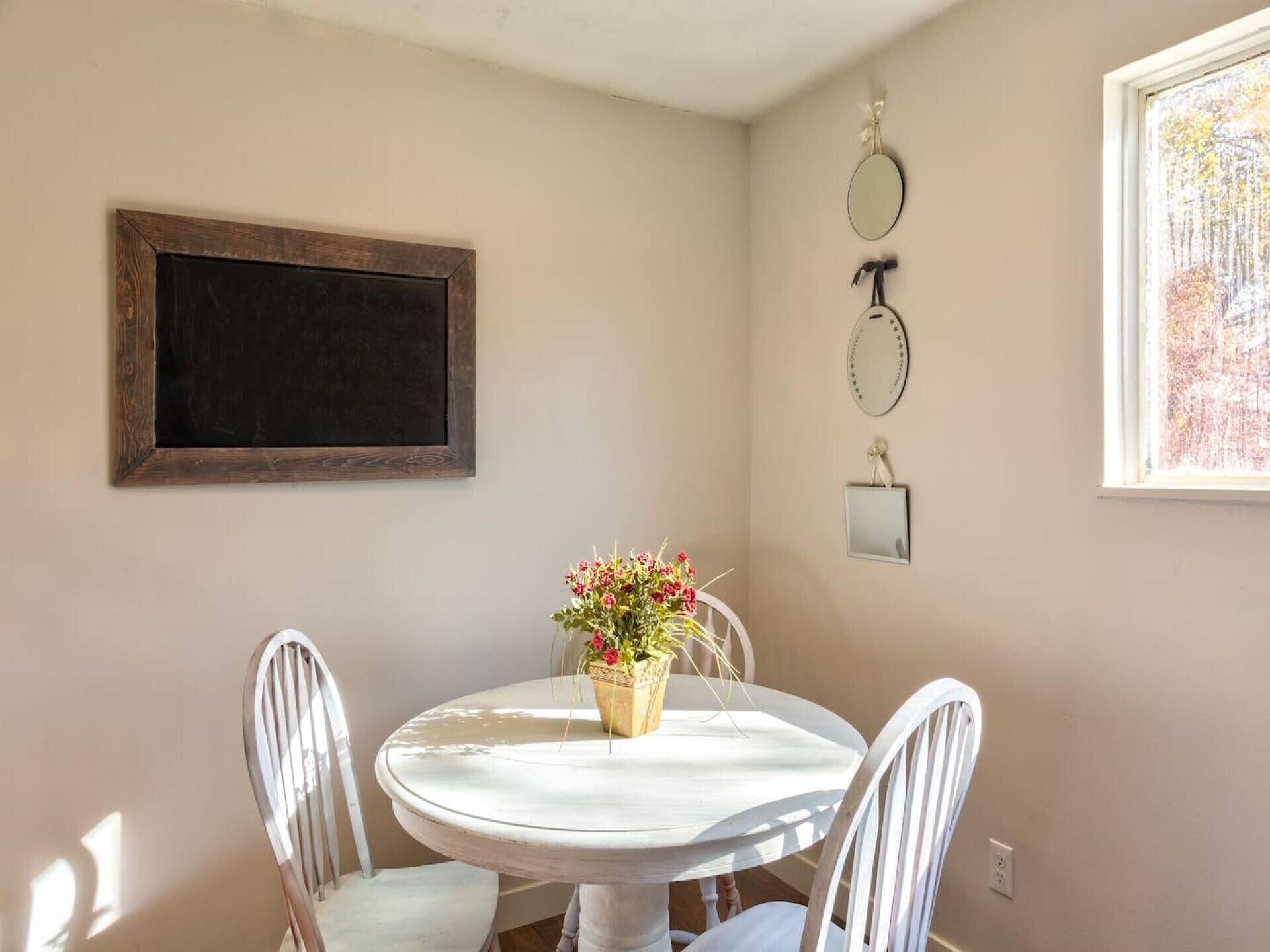 A dining area with a round table, two chairs, a potted plant, and wall-mounted mirrors.