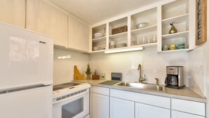 A modern kitchen with white cabinets, a built-in oven, a sink, and a coffee maker.