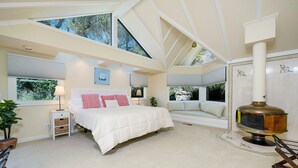 A bedroom with a large bed, a wooden chair, a fireplace, and a view of trees through skylights. - Beautiful Napa Valley Home on Golf Course -  Perfect Wine Country Retreat (Napa)
