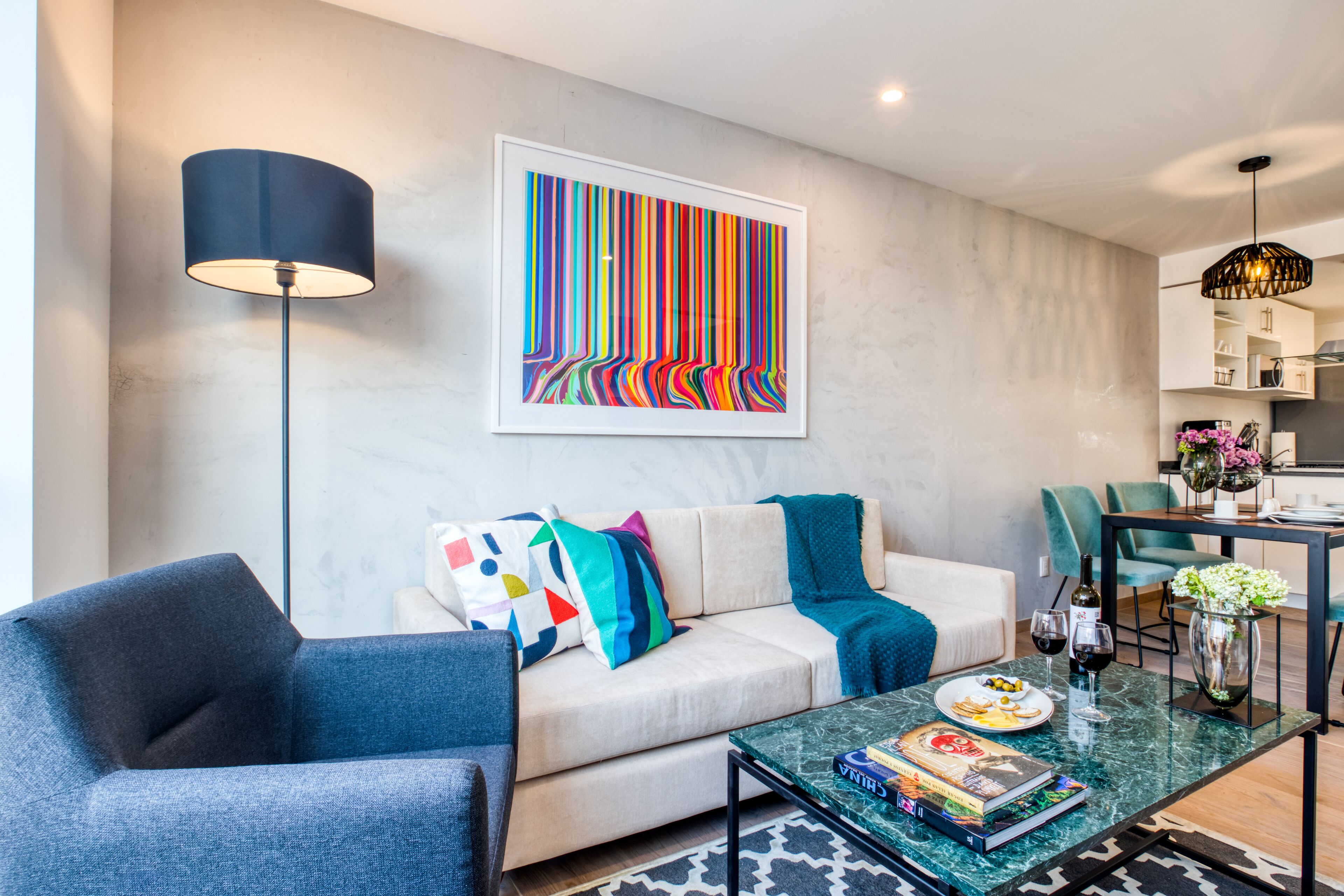 Una sala de estar moderna con sofá, sillón y mesa de centro, un comedor con sillas y una cocina al fondo.
