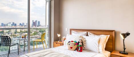 A hotel room with a large bed, a nightstand with a lamp, a chair, and a view of the city through a large window.