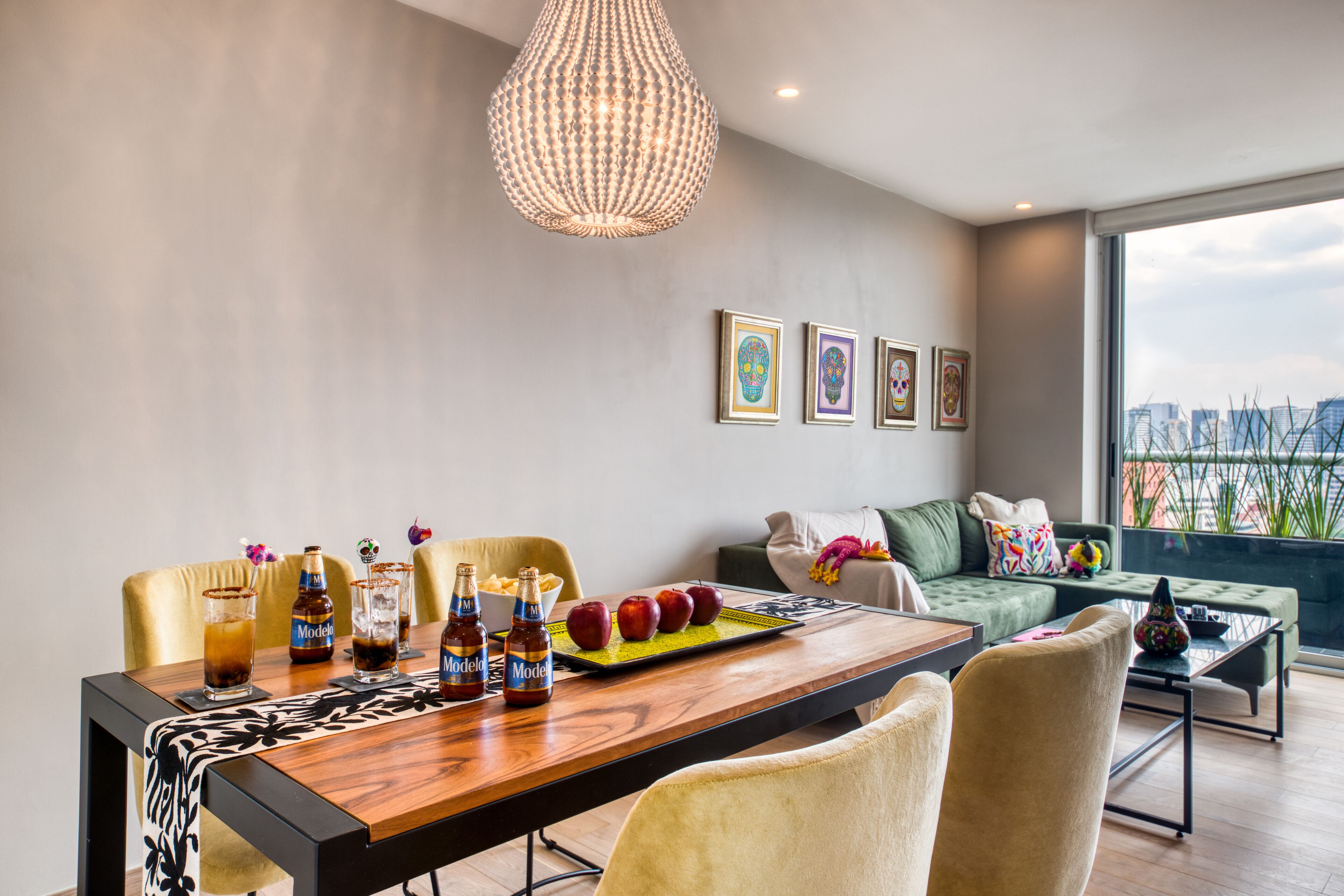 A modern living room with a dining area, featuring a wooden table, comfortable seating, a chandelier, and artwork on the wall.