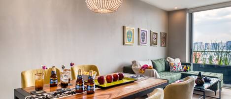 A modern living room with a dining area, featuring a wooden table, comfortable seating, a chandelier, and artwork on the wall.