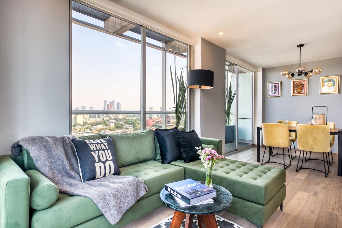 A modern living room with a green sofa, a round coffee table, and a dining area with yellow chairs.