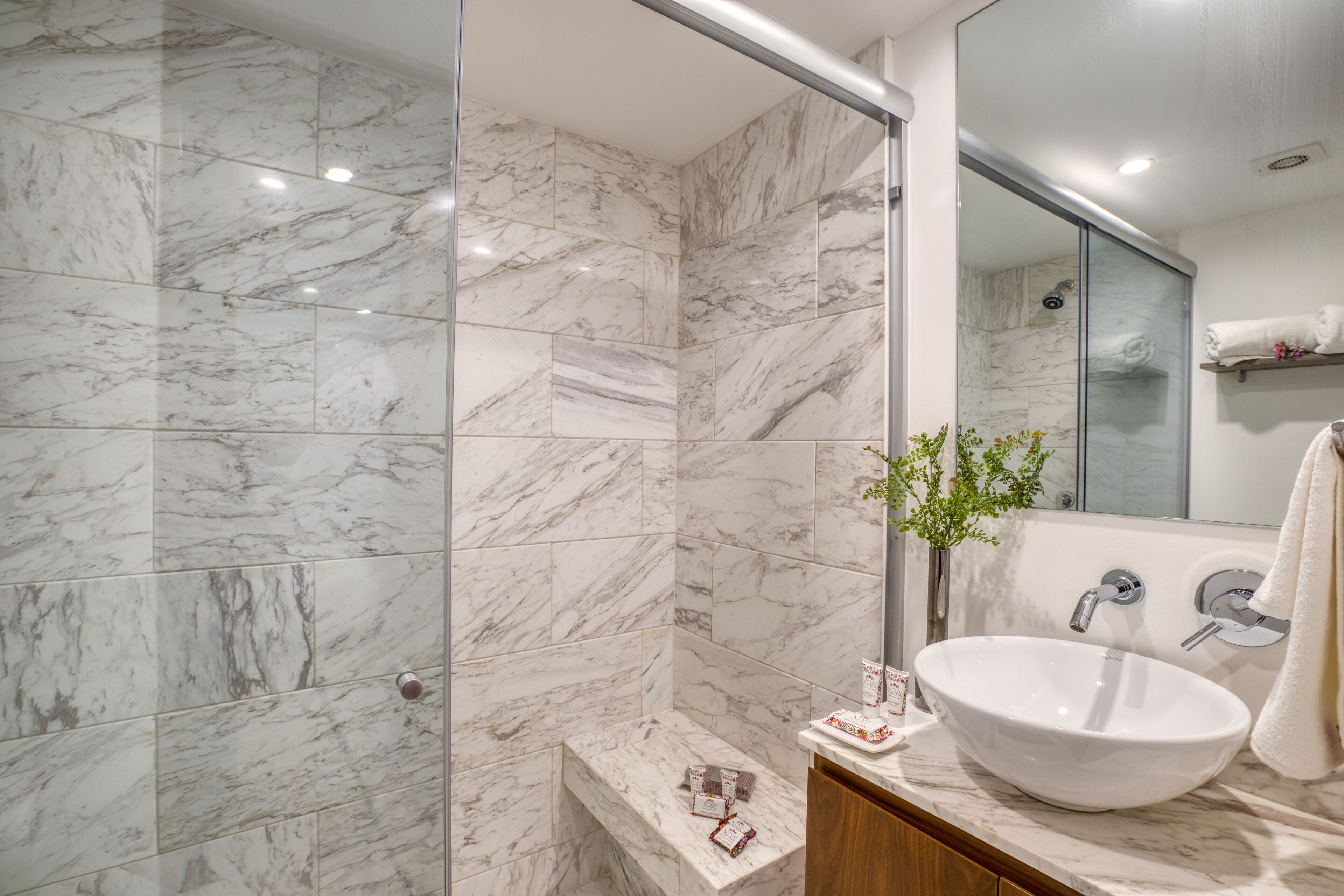 A modern bathroom with a marble shower, a white sink, and a mirror.