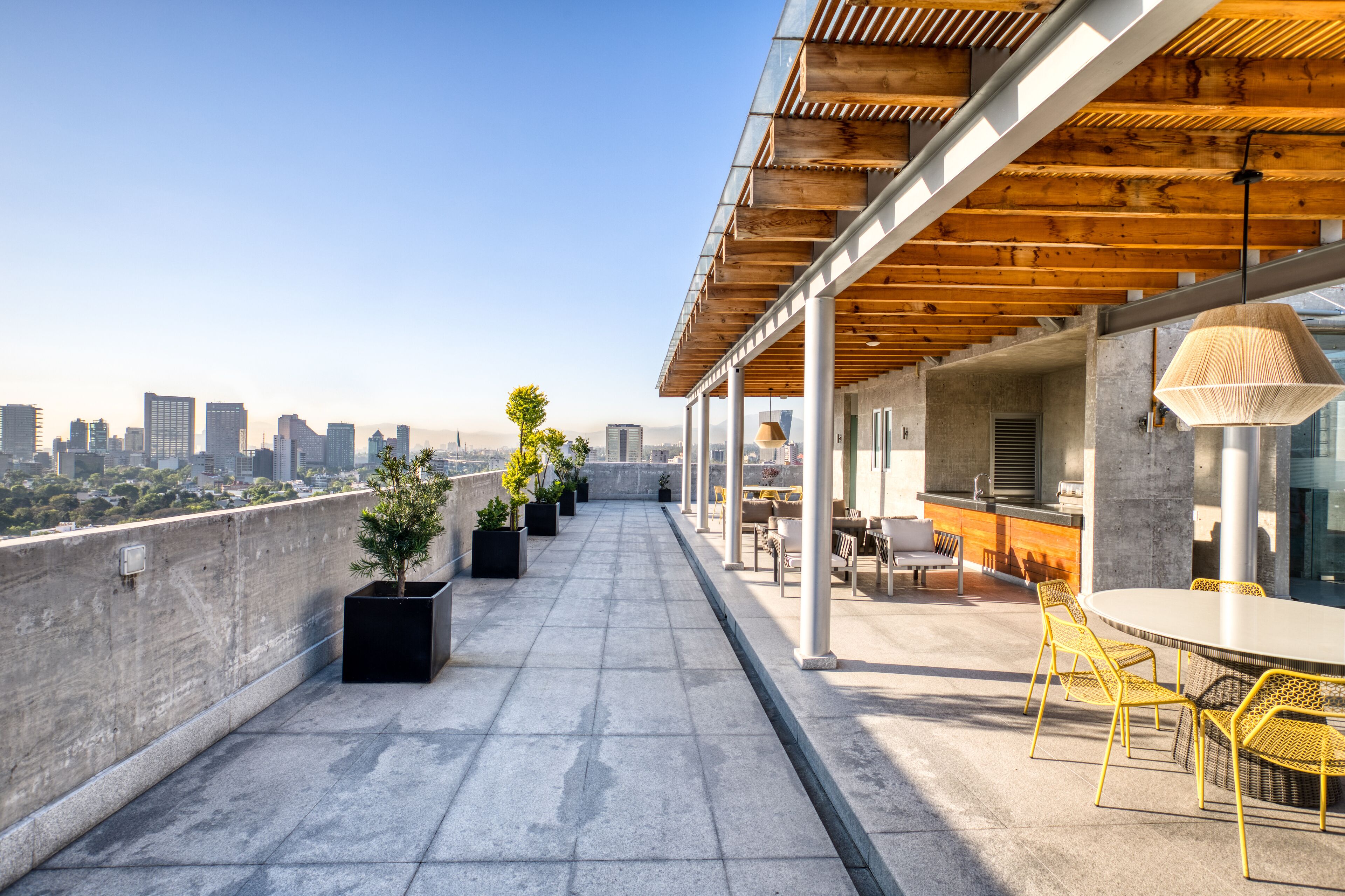 A rooftop terrace with a city view, outdoor seating, and potted plants.