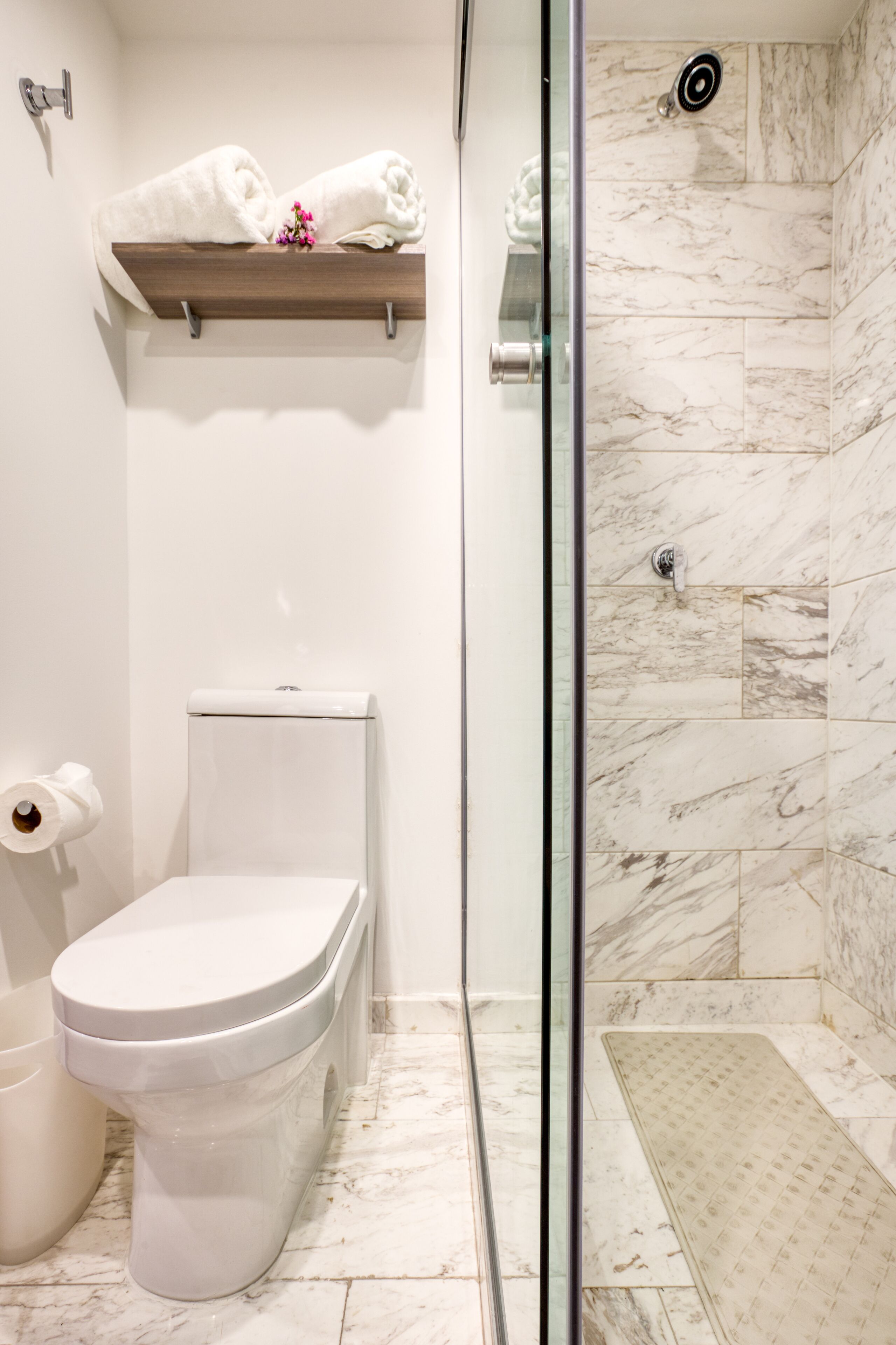 A bathroom with a toilet, a shower with a glass door, and a shelf with towels.