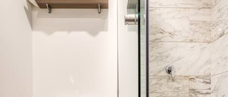 A bathroom with a toilet, a shower with a glass door, and a shelf with towels.