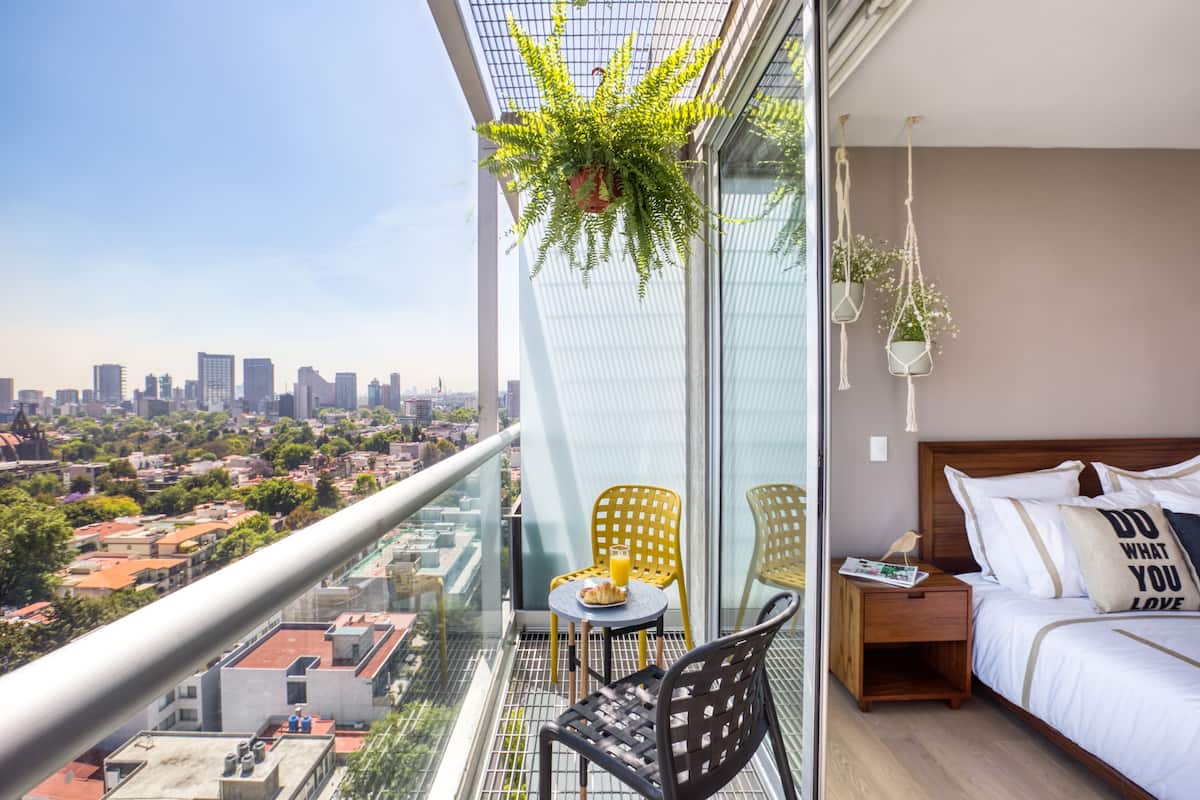 A balcony with a city view, a bed with a pillow saying 'DO WHAT YOU LOVE', and a table with a plate of food.