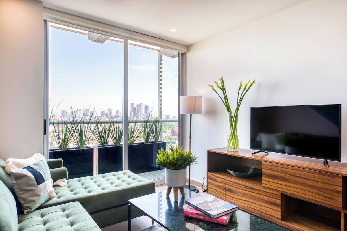 A modern living room with a large window, a green sofa, a coffee table, a TV, and a potted plant.