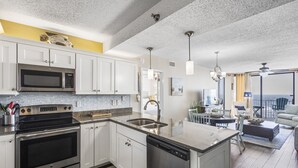 A modern kitchen with stainless steel appliances, a dishwasher, and a large island. There is a dining area with a view of the ocean.