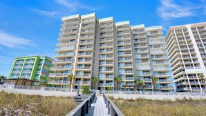 A multi-story hotel with balconies, a covered walkway, and a beach view.
