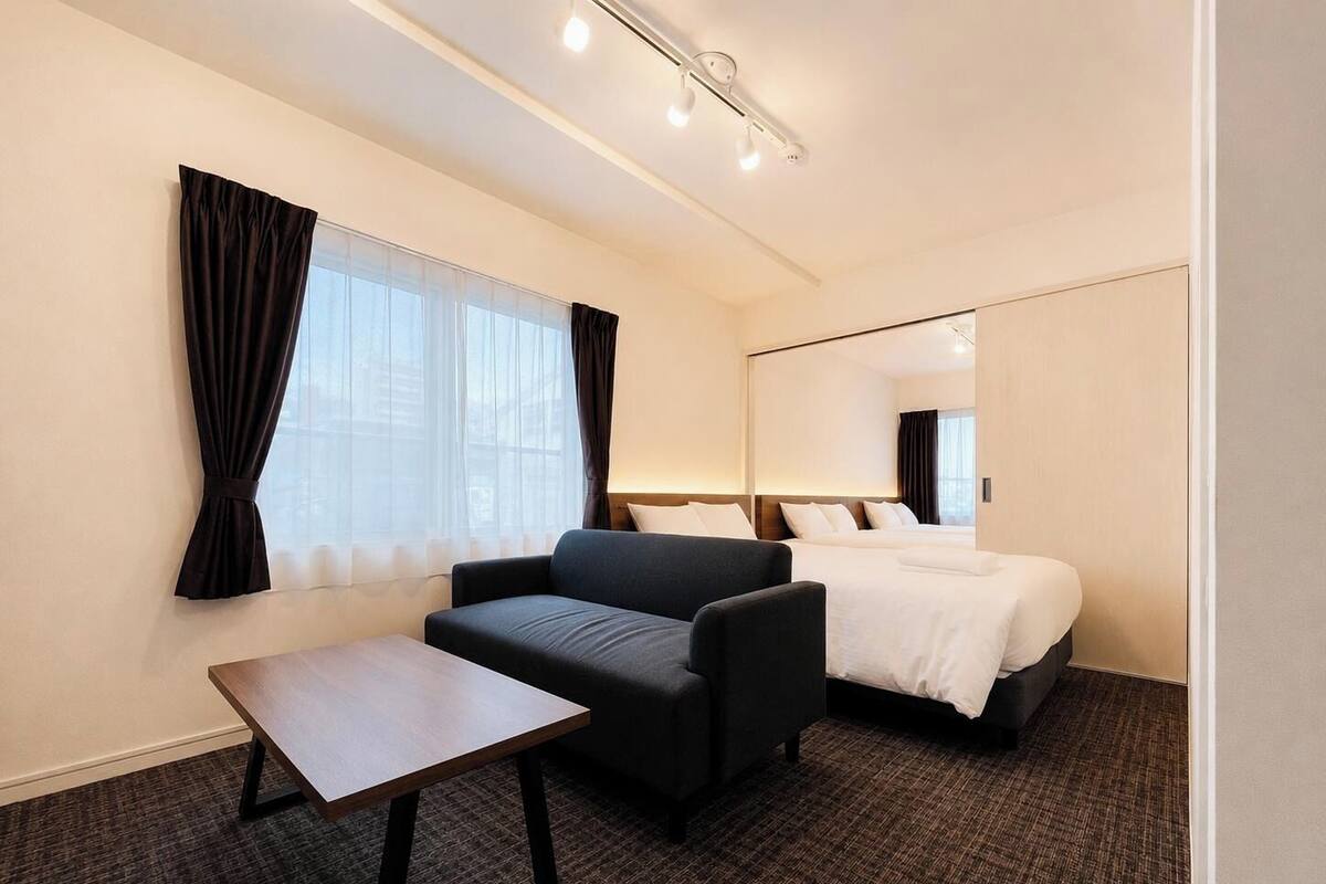 A hotel room with a bed, a sofa, a small table, and a large mirror.
