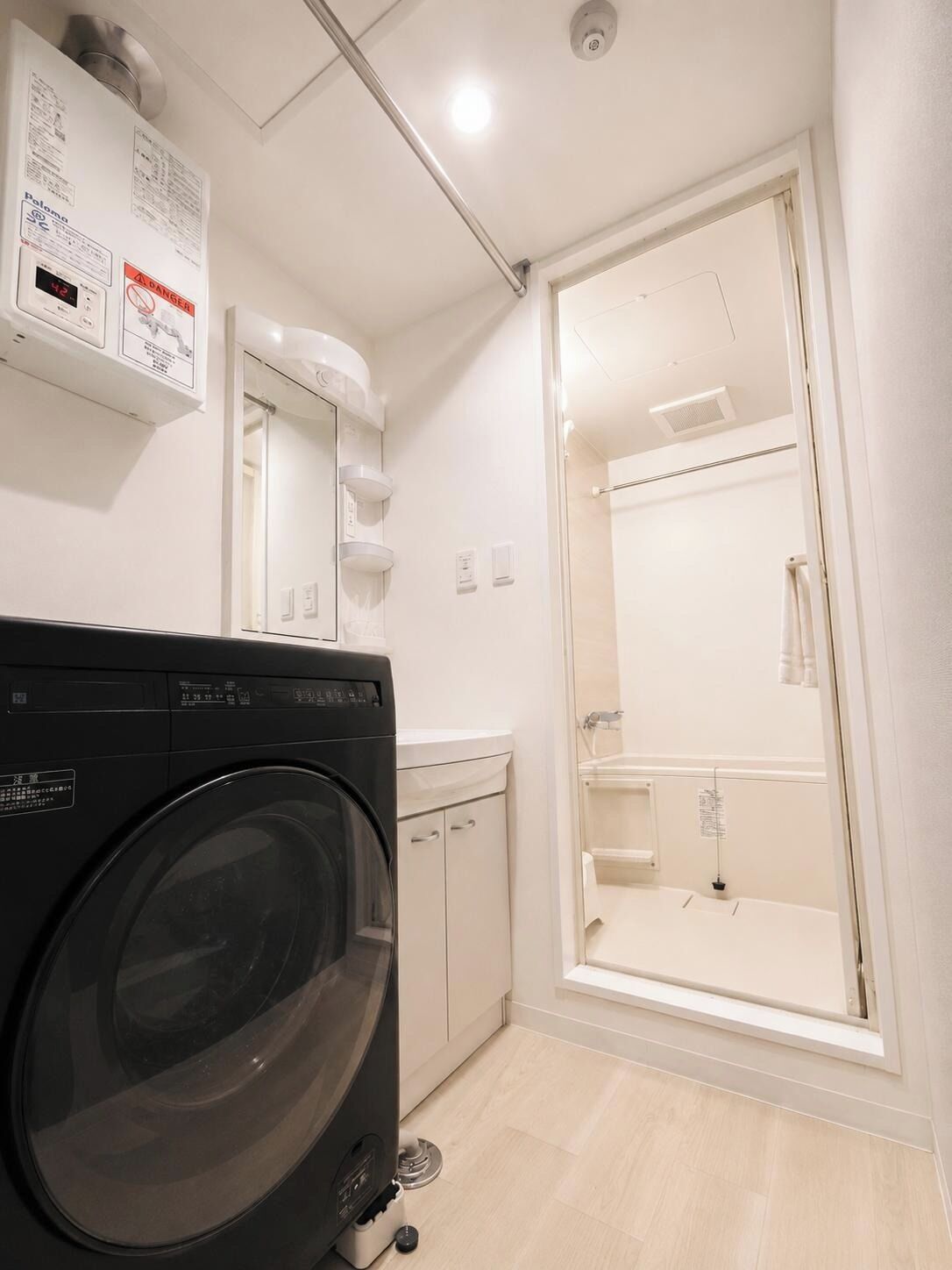 A compact hotel bathroom with a washing machine, a glass shower enclosure, and a toilet.