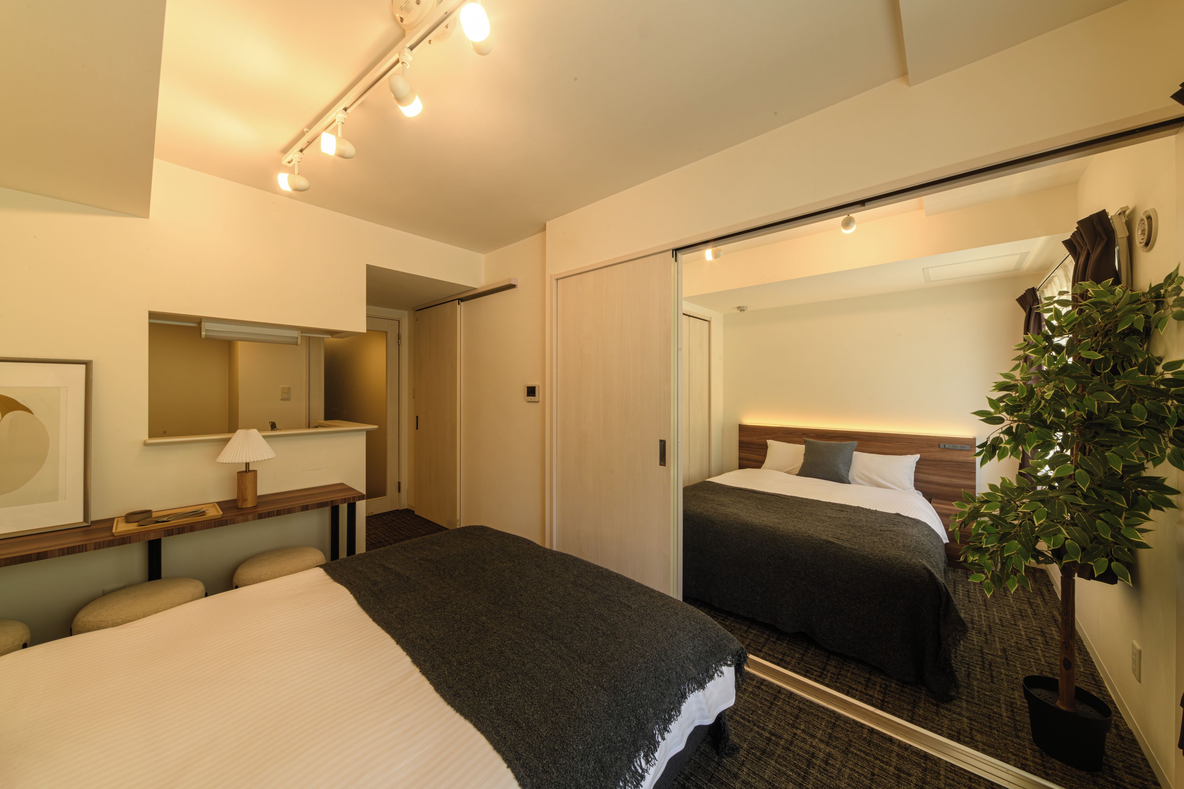 A hotel room with a bed, bedside table, lamp, mirror, and a potted plant.