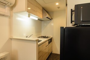 A compact kitchen with a built-in stove, a sink, and a black refrigerator. - Hotel ONE'S RESIDENCE (Sapporo)