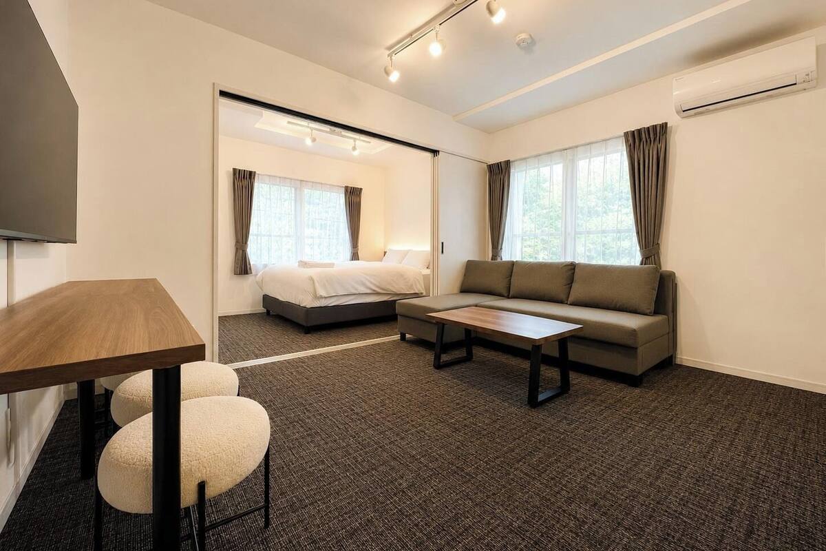 A modern hotel room with a bed, sofa, coffee table, and a TV.