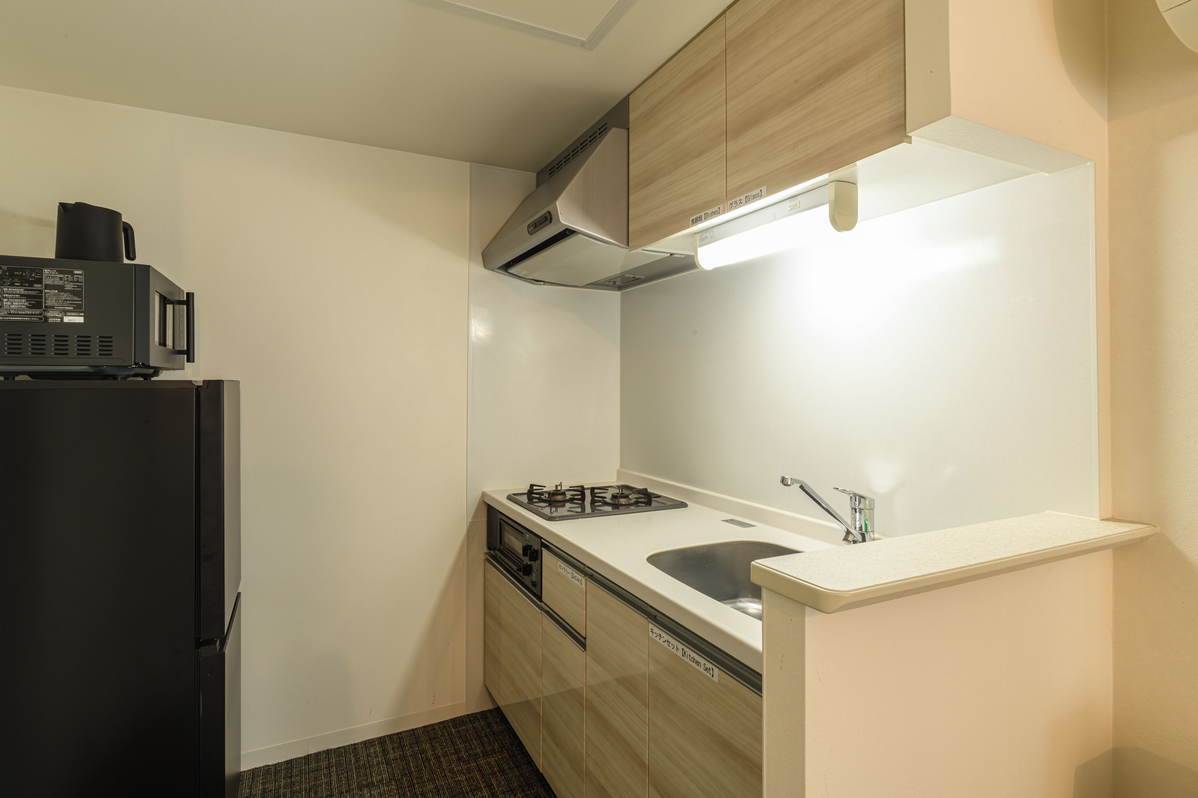 A compact kitchen with a black refrigerator, a stove, and a microwave.