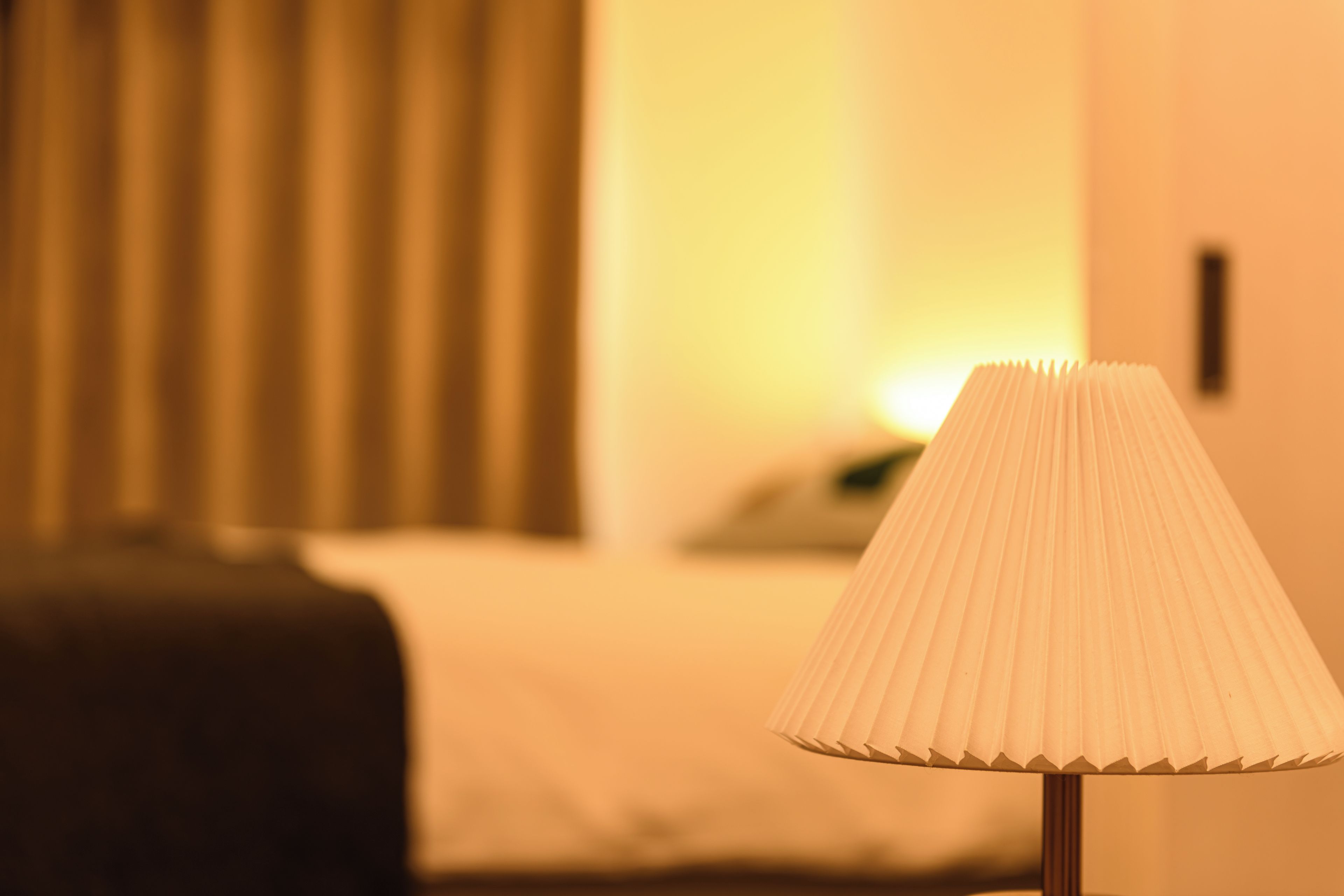 A lamp with a pleated shade on a bedside table in a hotel room.