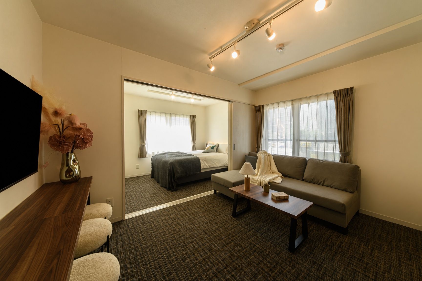 A hotel room with a bed, sofa, TV, and a desk with a lamp.