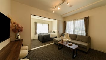 Habitació d'hotel amb llit, sofà, televisió i escriptori amb làmpada.