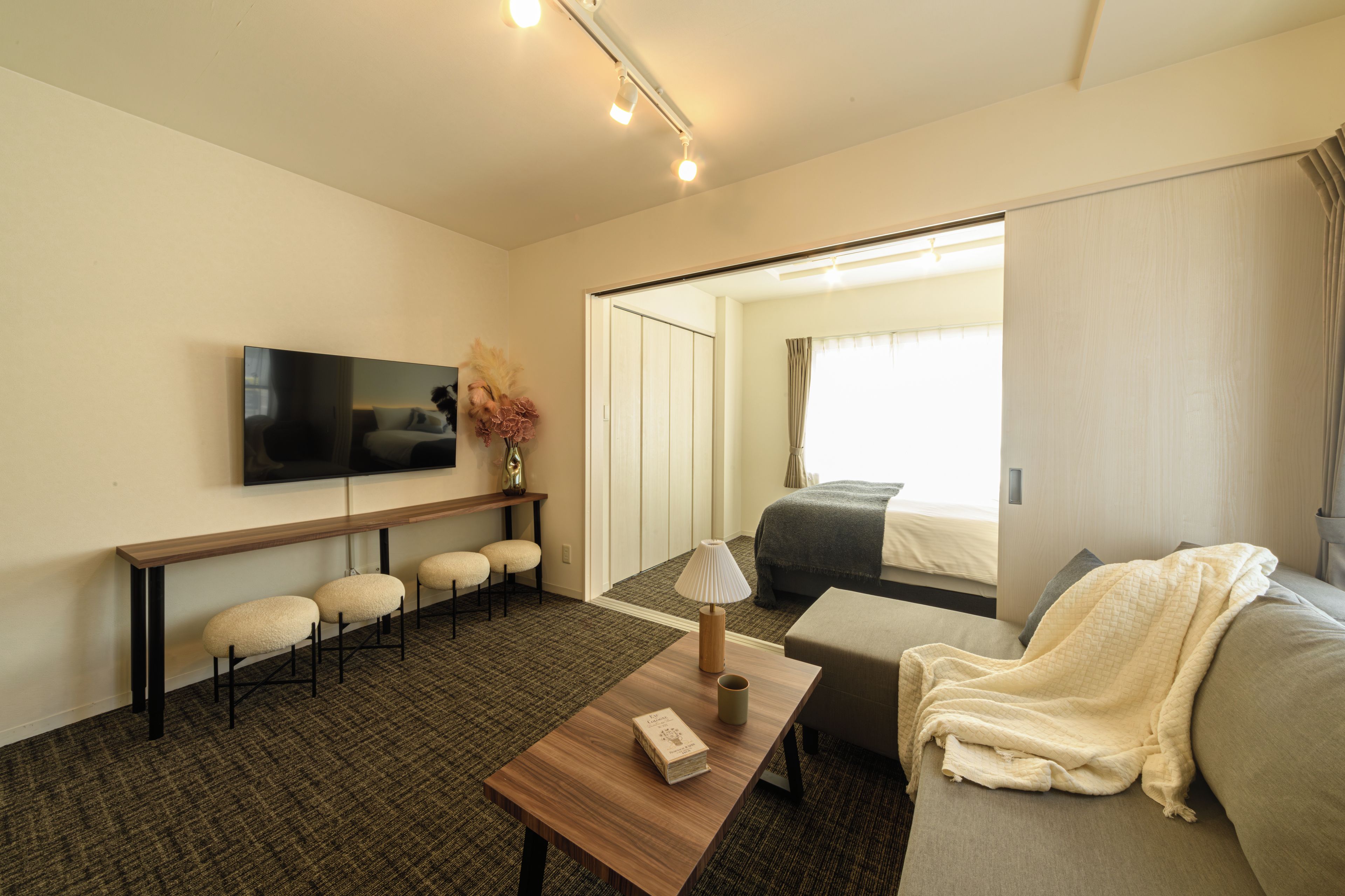 A hotel room with a flat-screen TV, a sofa, a coffee table, and a mirror reflecting the bed and window.