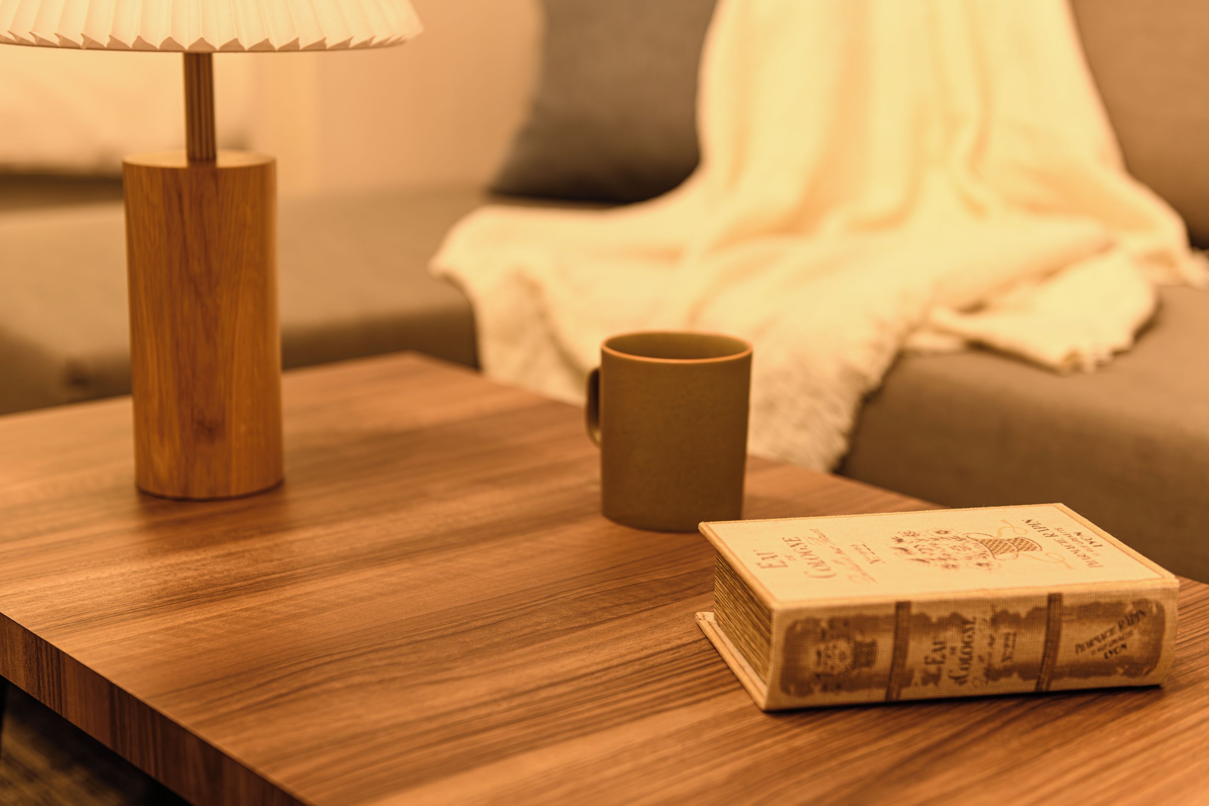 A wooden bedside table with a lamp, a mug, and a book.