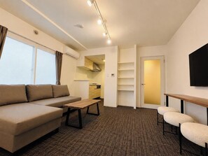 A modern living room with a sofa, a coffee table, a TV, and a kitchen area. - Hotel ONE'S RESIDENCE (Sapporo)