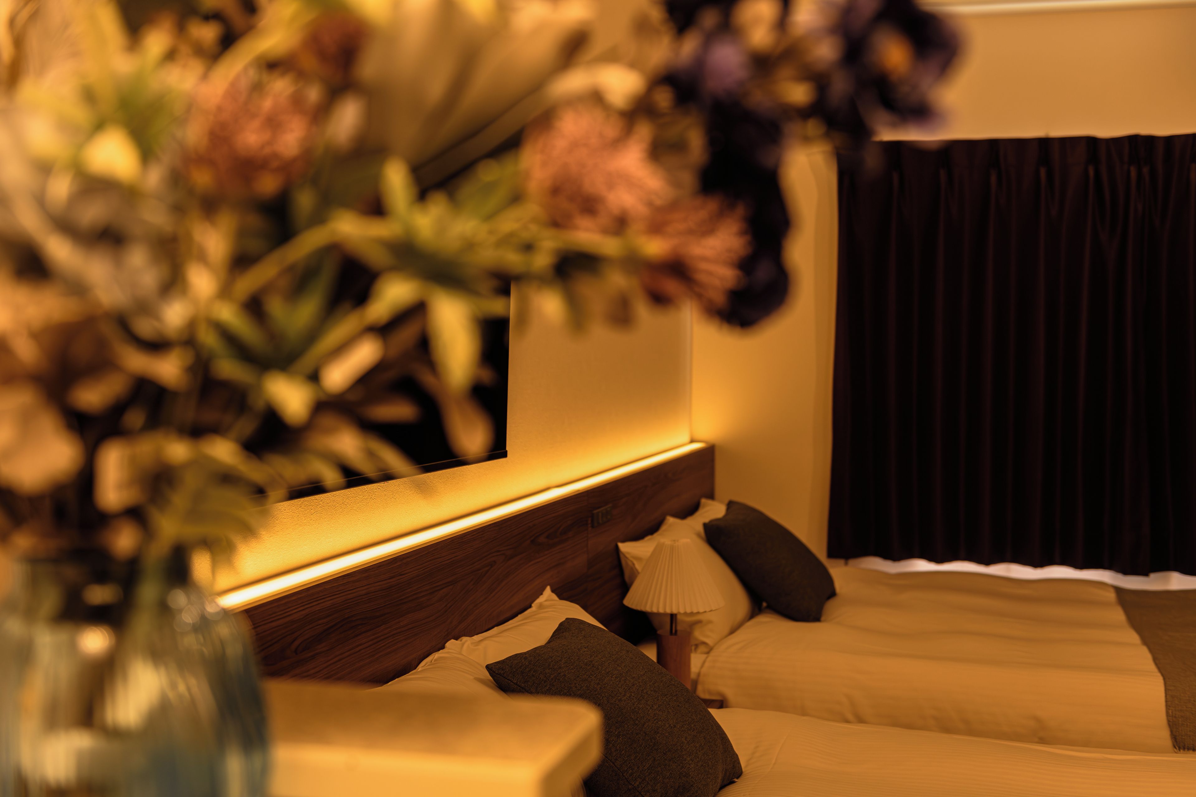 Una habitación de hotel con una cama, una mesita de noche, una lámpara y un florero con flores.