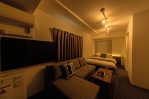 A hotel room with a sofa, a bed, a TV, and a bedside table with a lamp. - Hotel ONE'S RESIDENCE (Sapporo)