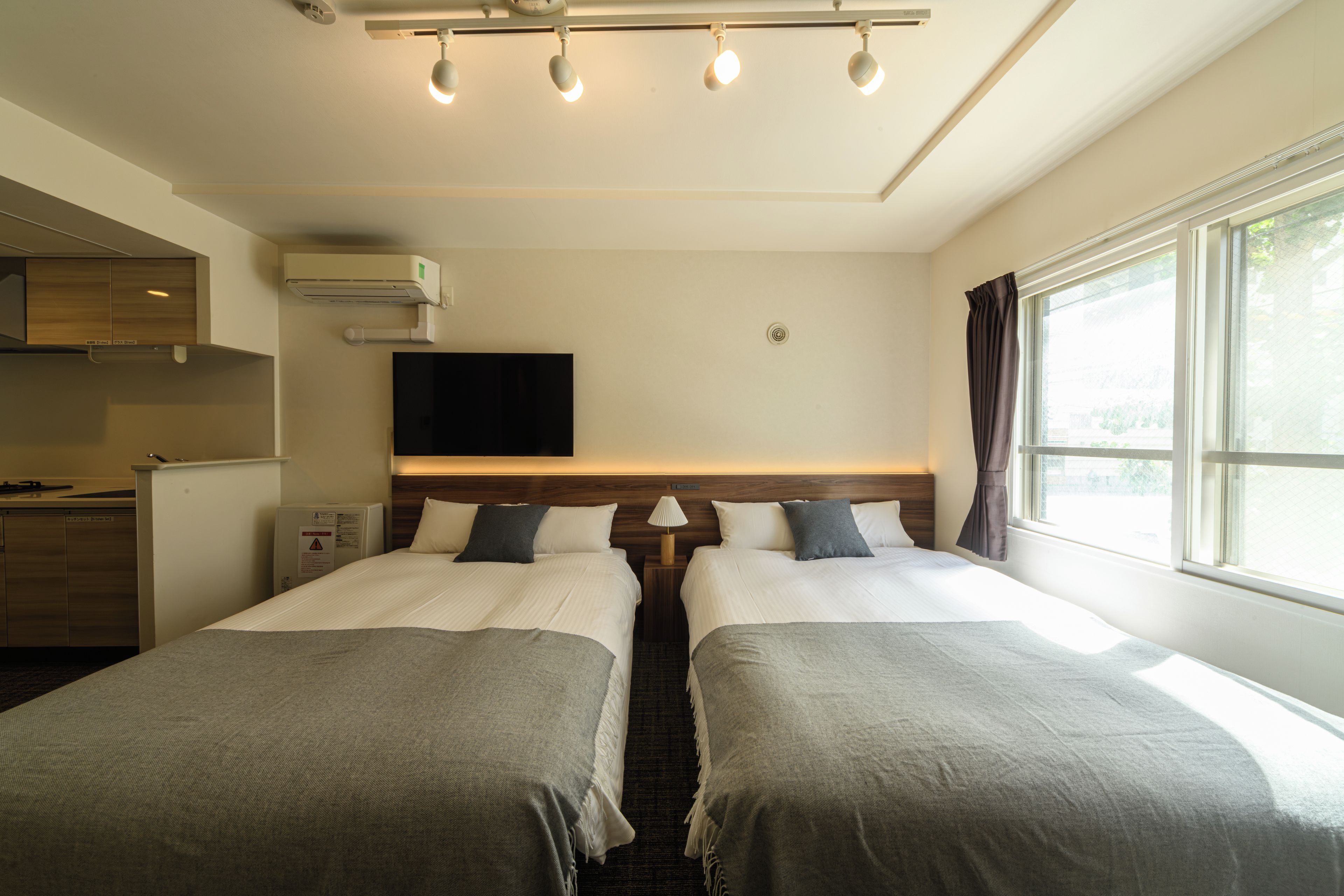 A hotel room with two beds, a TV, a window with curtains, and a kitchenette.