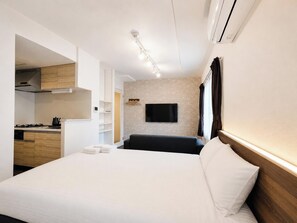 Une chambre d’hôtel moderne équipée d’un lit, d’un téléviseur à écran plat fixé au mur, d’une kitchenette avec une cuisinière et d’un appareil de climatisation installé au plafond.