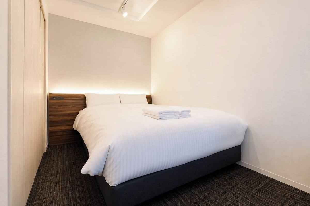 A hotel room with a bed, a wooden headboard, a carpeted floor, and a ceiling light fixture.
