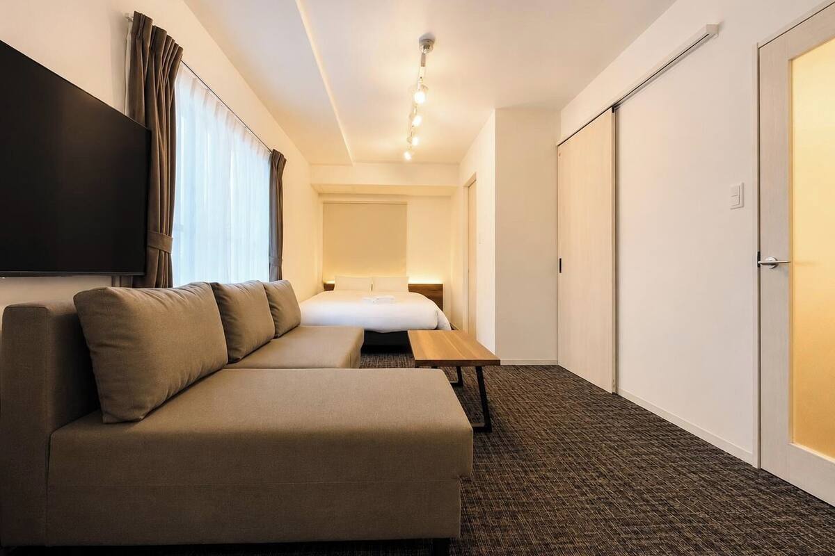 A hotel room with a sofa, a bed, a flat-screen TV, and a door.