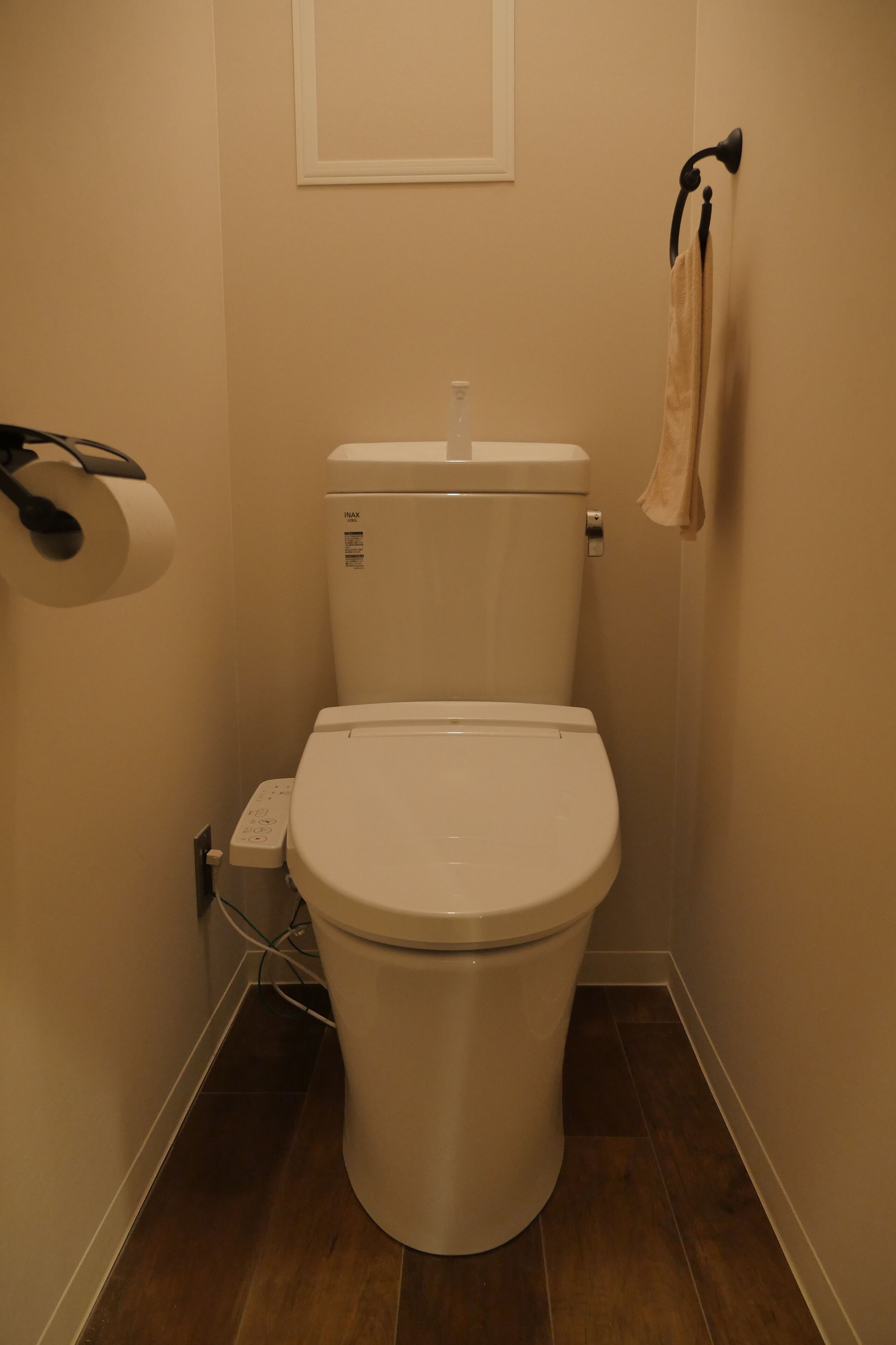 A small bathroom with a white toilet, a roll of toilet paper, and a towel hanging on a rack.